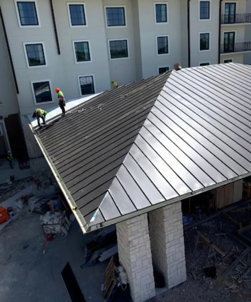 Crew installing standing seam metal roof panels on a commercial project in Corning